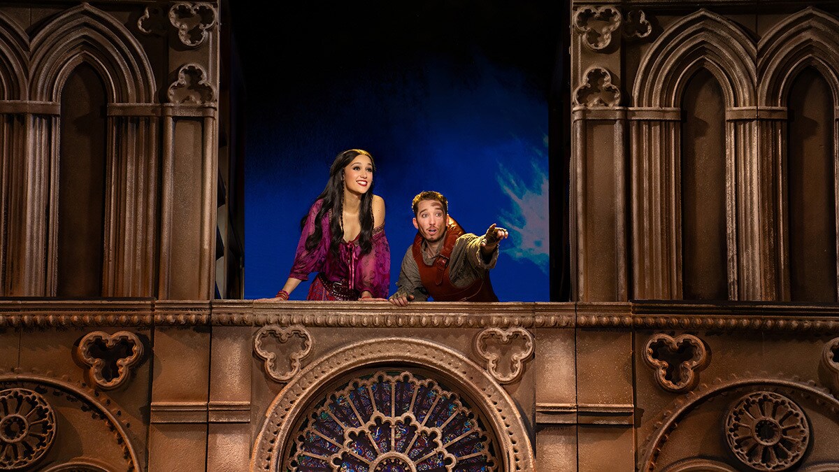 Quasimodo steht gemeinsam mit Esmeralda auf den Dächern von Notre Dame und deutet mit seinem Arm in die Ferne.