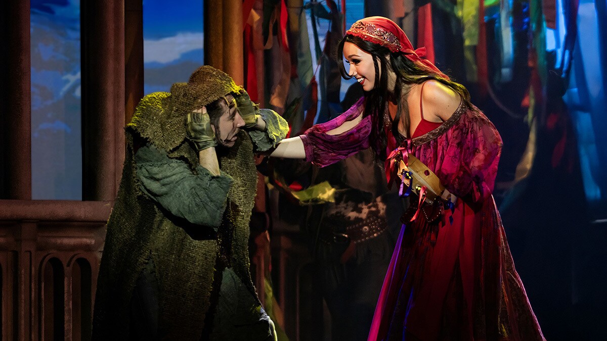 Esmeralda und Quasimodo treffen aufeinander. Er ist verschleiert in alter und verdreckter Kleidung und schaut interessiert zu ihr hoch.