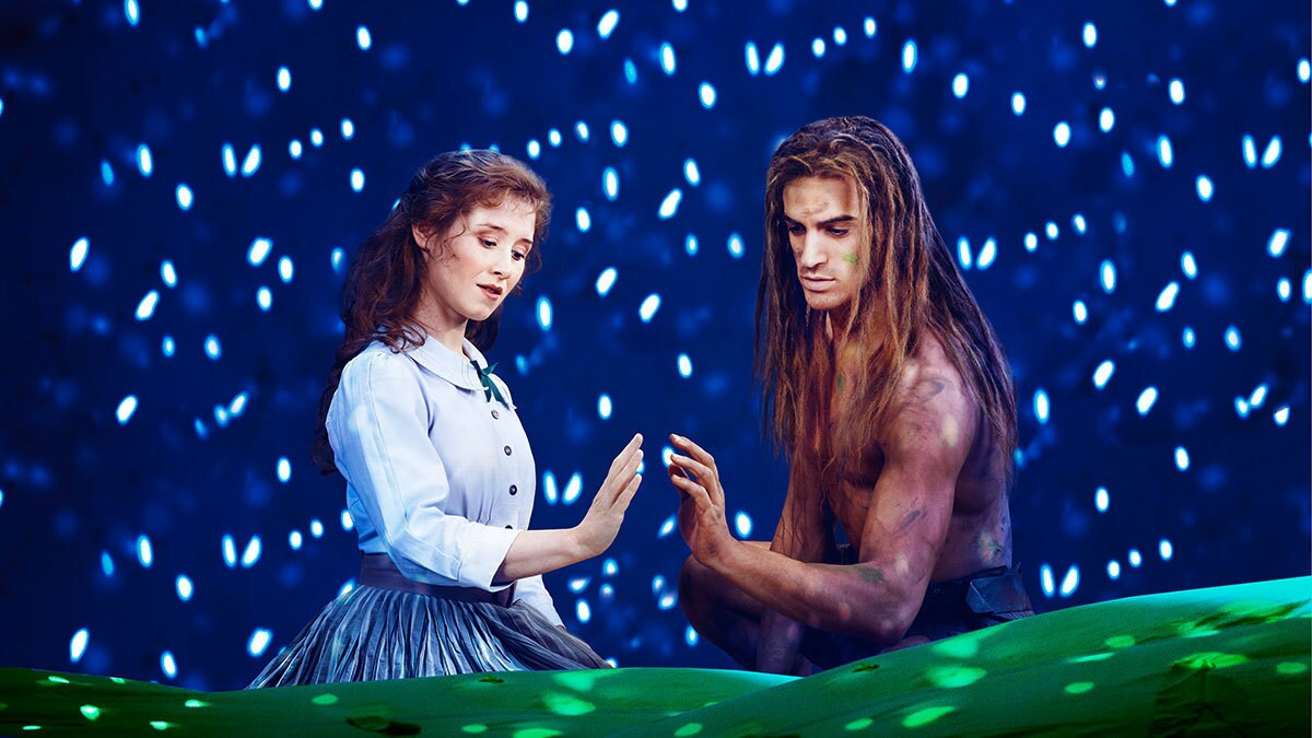 Jane und Tarzan sitzen sich vor einem Sternenhintergrund gegenüber und halten ihre Hände aneinander.