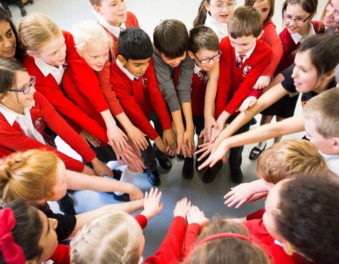 School children in a circle putting their hands out in front of them