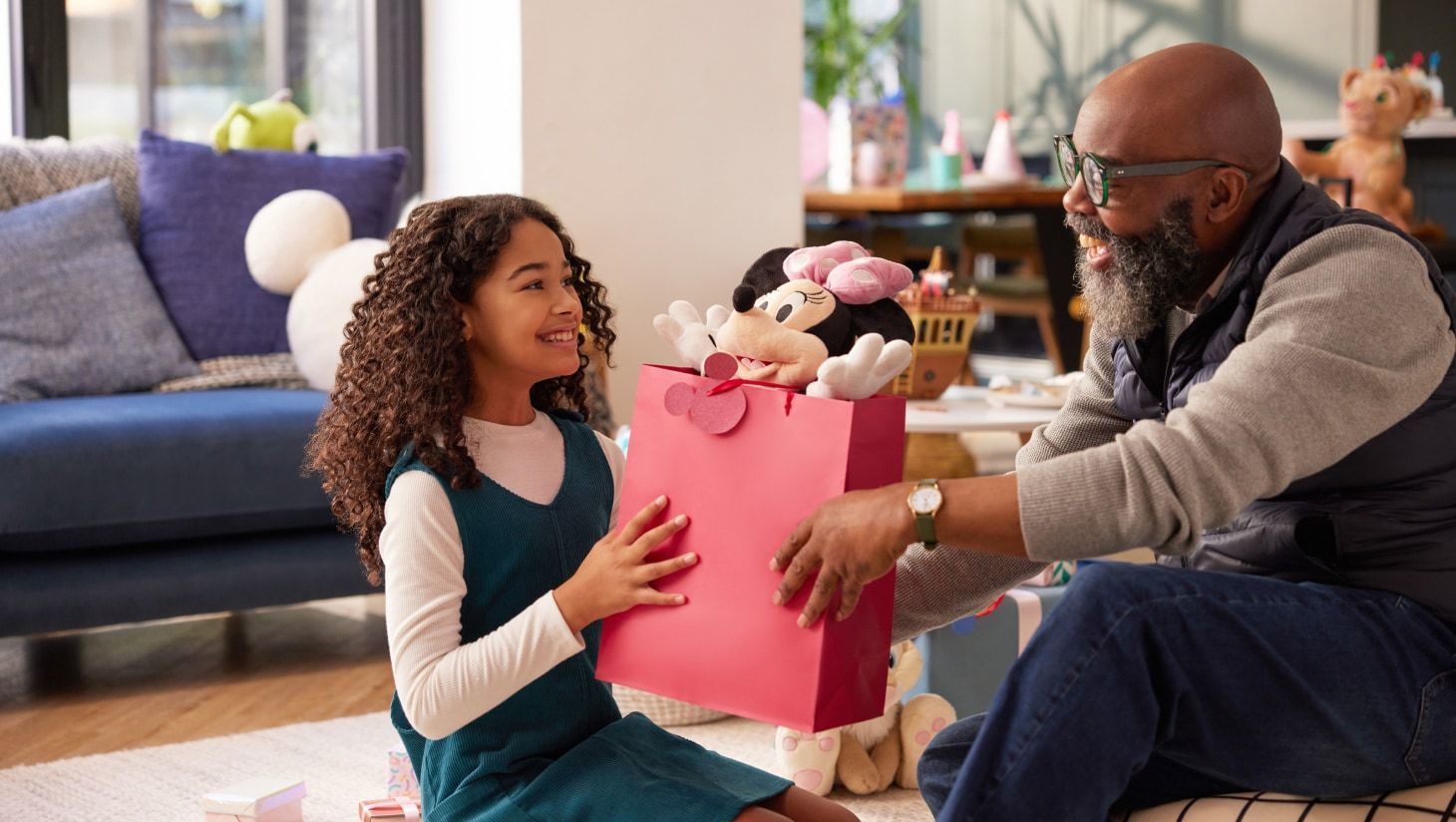 Ein Mann reicht einem Kind eine Geschenktüte mit einem Minnie-Plüsch