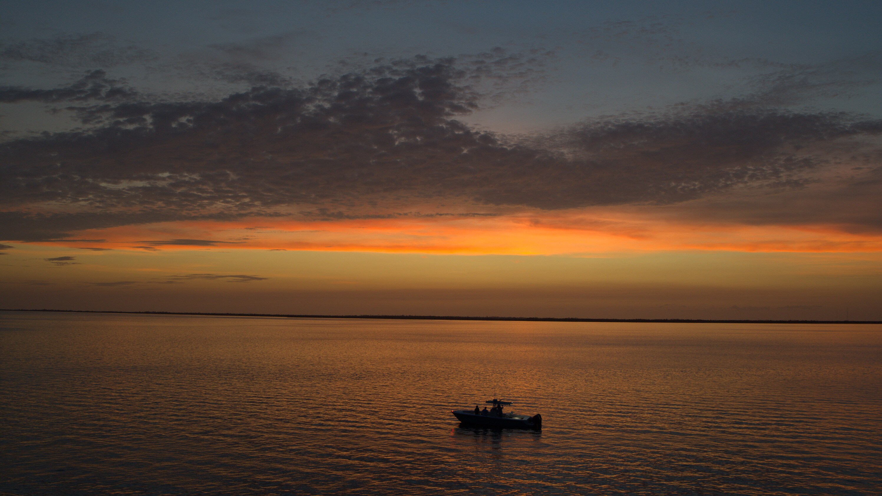 A boat out on the ocean side of the Florida Keys, against an orange sunset. (National Geographic for Disney+)