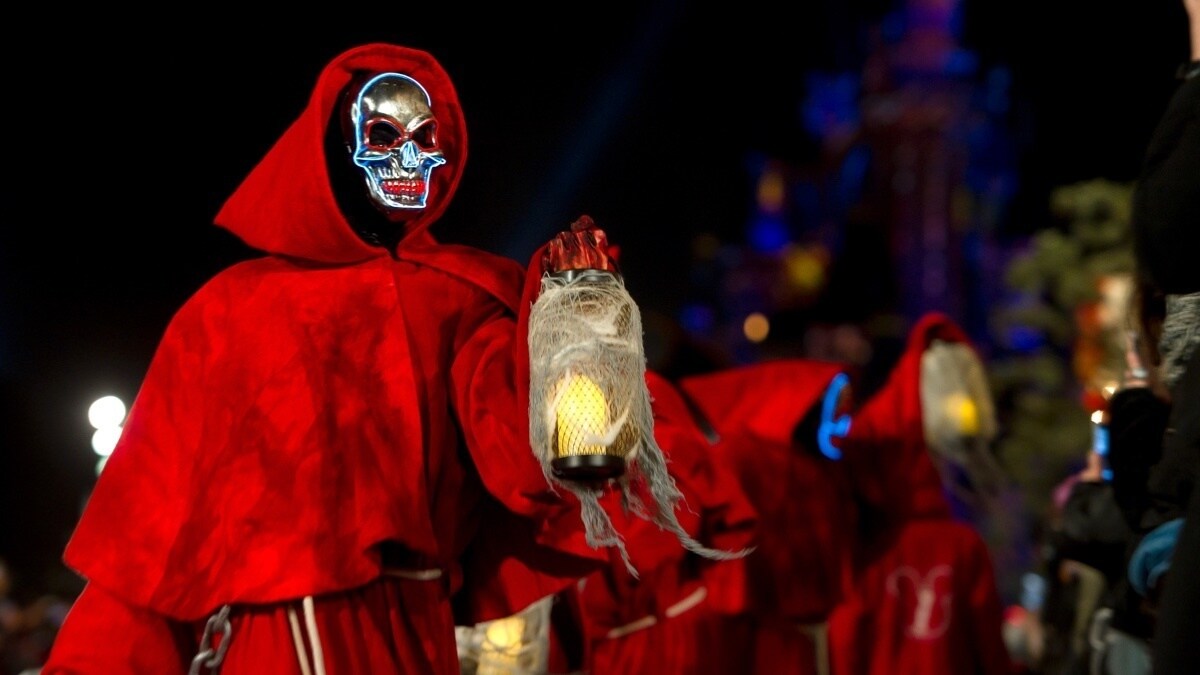 Person in hooded outfit with a skeleton mask holding a lantern