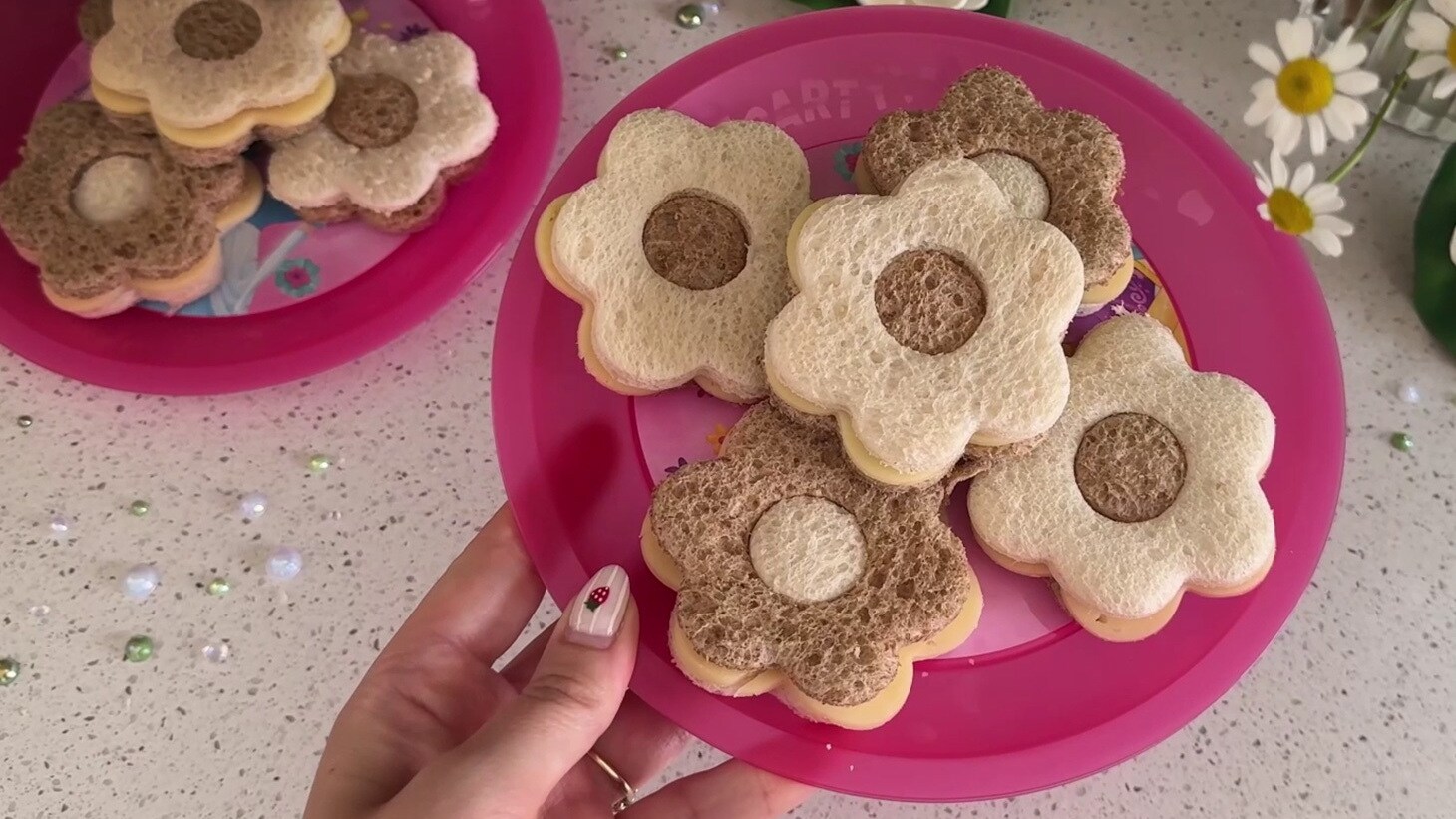Flower-shaped sandwiches inspired by Tiana from Disney’s The Princess and the Frog, featuring a pink plate with white and brown bread sandwiches.