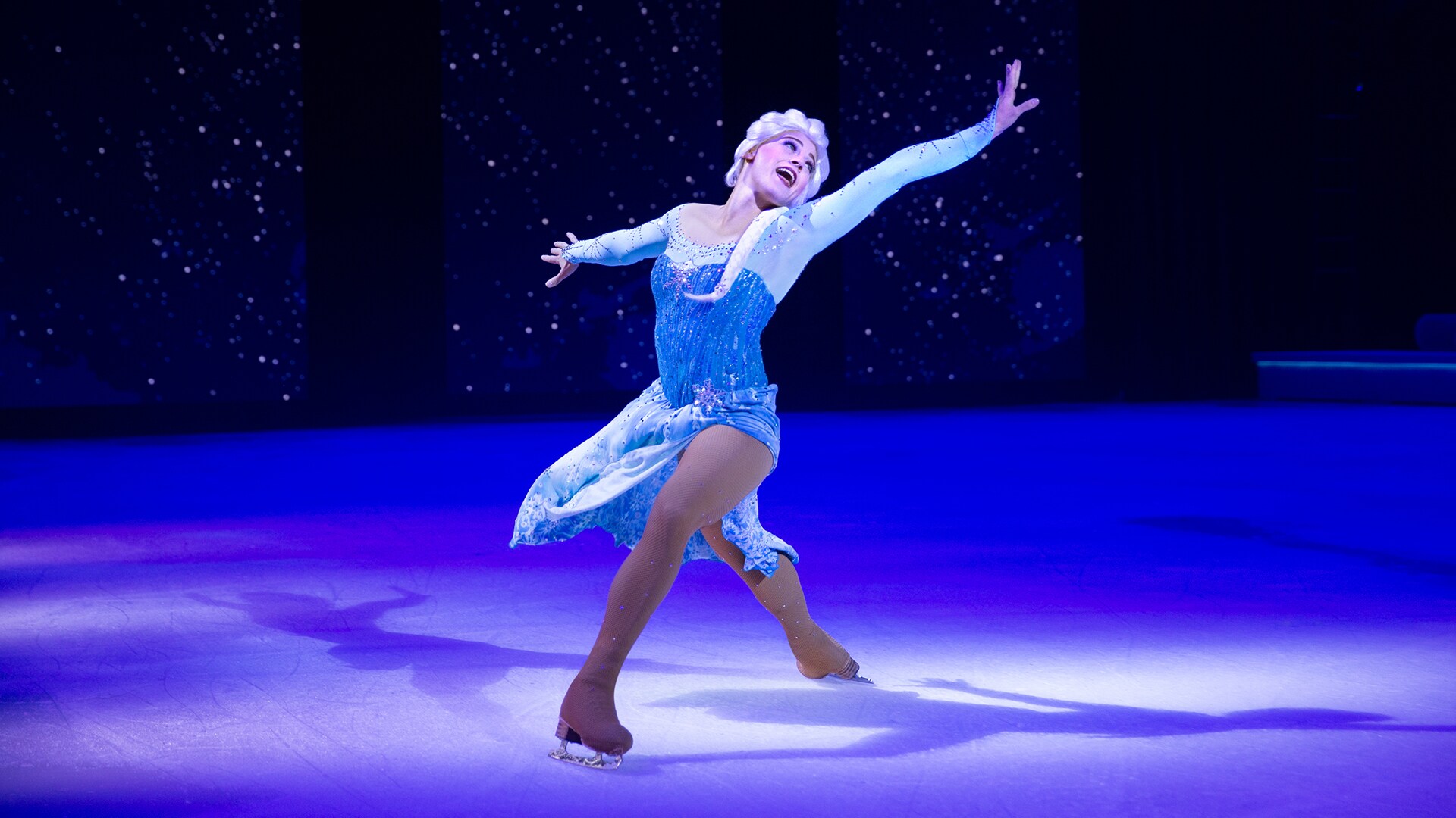 Elsa on a spotlight while singing and dancing on ice with her arms spread to the sides.