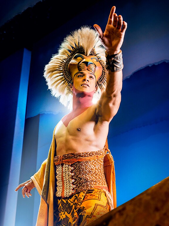 Actor who plays Simba, in costume looking to the distance and reaching out to the front with his hand