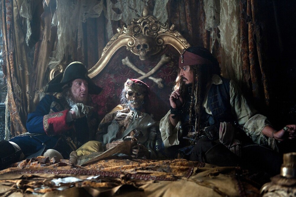 Captain Barbosa, and Captain Jack Sparrow sitting next to a skeleton