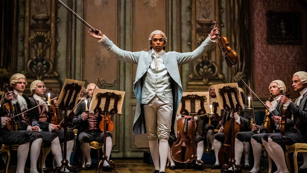 Joseph (actor Kelvin Harrison Jr.), raises his arms holding a violin in one and the bow in another in the 20th Century Studios movie, "Chevalier."