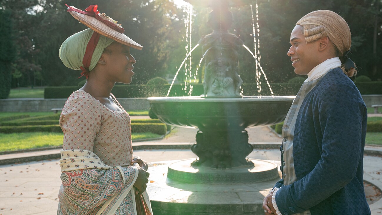 Nanon (actor Ronke Adekoluejo) and Joseph (actor Kelvin Harrison Jr.) in front of an outdoor fountain from the 20th Century Studios movie, "Chevalier."