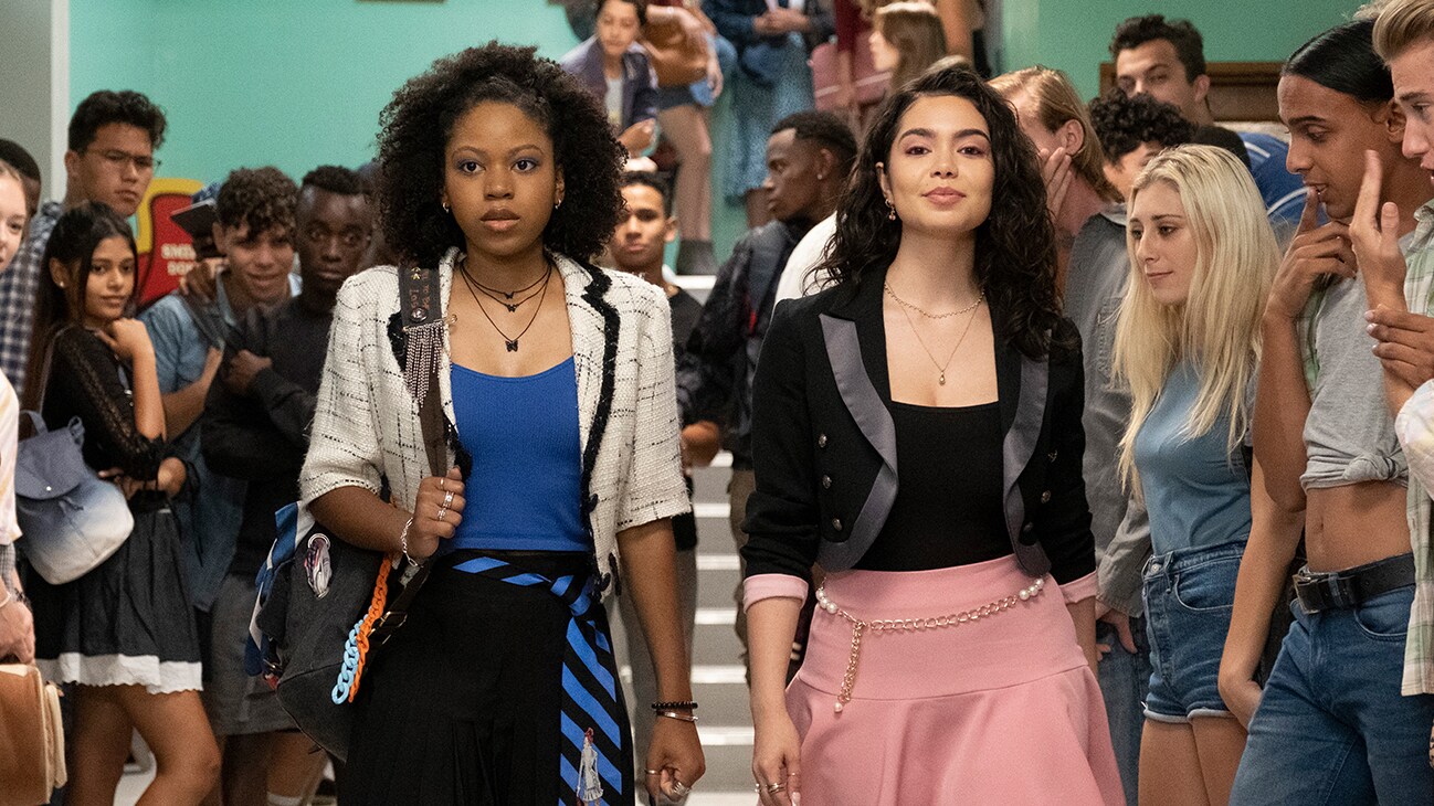 Image of Darby Harper (actor Riele Downs) and Capri (actor Auli'i Cravalho) walking down a classroom hallway, from the 20th Century Studios movie, "Darby and the Dead".
