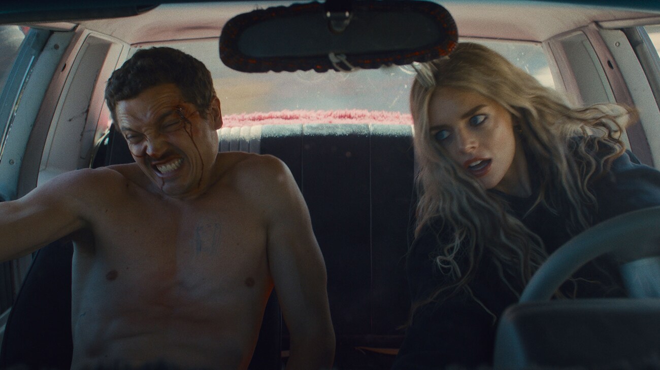 Edie (Samara Weaving) driving erratically with John (Karl Glusman) in the passenger seat in a scene from 20th Century Studios' EENIE MEANIE. Photo courtesy of 20th Century Studios. © 2025 20th Century Studios. All Rights Reserved.