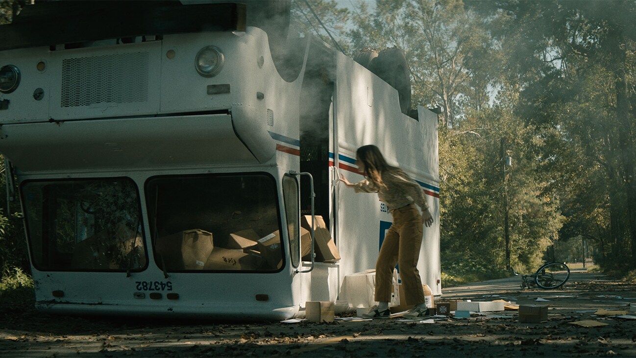 Actor Kaitlyn Dever inspecting an overturned post office vehicle in the 20th Century Studios movie, "No One Will Save You."