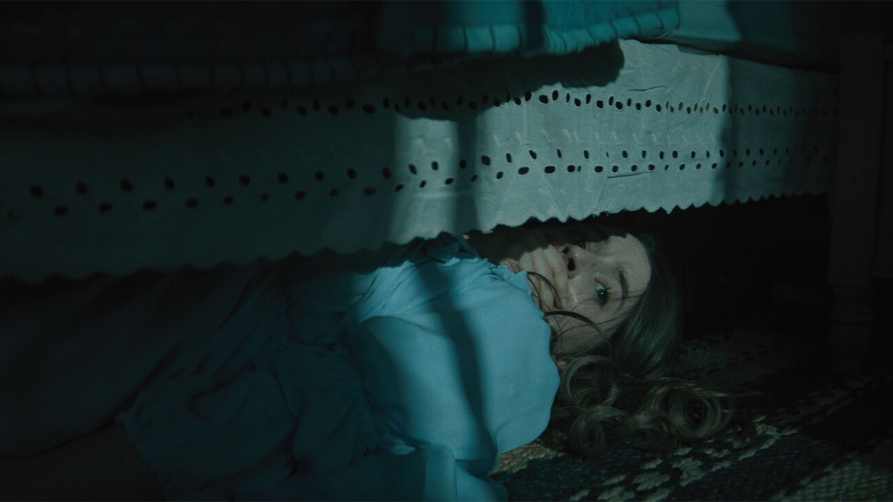 Actor Kaitlyn Dever underneath a bed in the 20th Century Studios movie, "No One Will Save You."