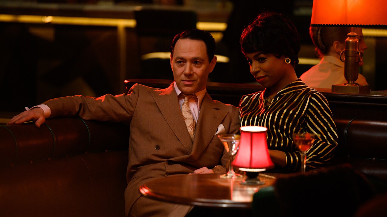 John Woolf (actor Reece Shearsmith) and Ann Saville (actor Pippa Bennett-Warner) sitting at a table from the Searchlight Pictures movie, "See How They Run".