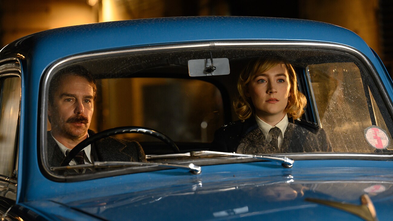 Inspector Stoppard (actor Sam Rockwell) and Constable Stalker (actor Saoirse Ronan) in a car from the Searchlight Pictures movie, "See How They Run".