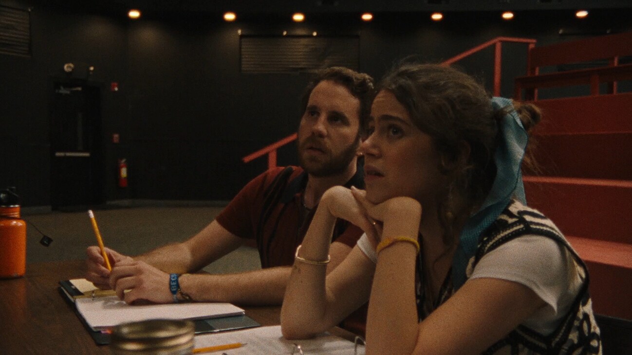 Molly Gordon and Ben Platt sitting at a table from the Searchlight Pictures movie, "Theater Camp."