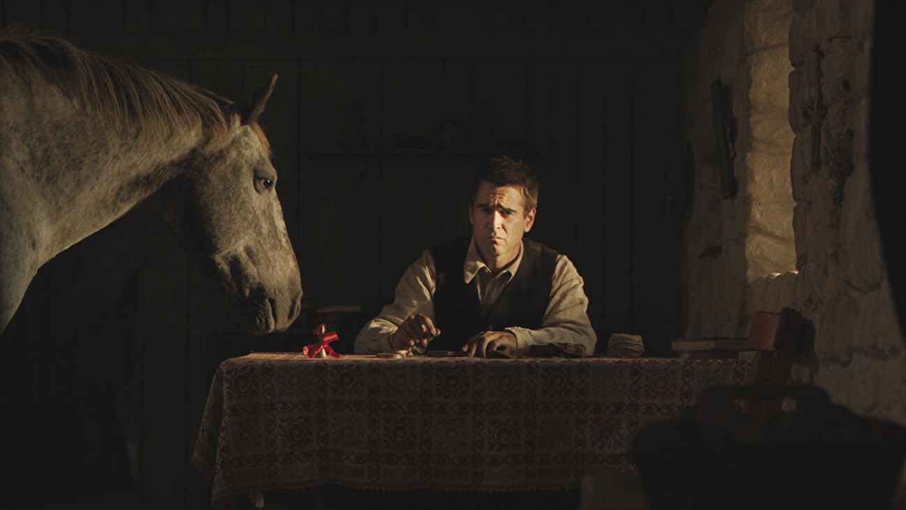 Pádraic Súilleabháin (actor Colin Farrell) sitting at a table with a horse from the Searchlight Pictures movie "The Banshees of Inisherin".