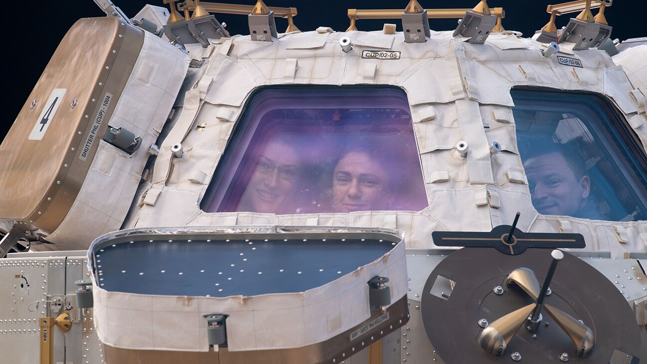 AMONG THE STARS - (Nov. 4, 2019) - NASA astronauts (from left) Christina Koch, Jessica Meir and Andrew Morgan peer through the International Space Station's "window to the world," the cupola. The trio were on robotics duty monitoring the arrival and capture of the Cygnus space freighter from Northrop Grumman. (NASA)  CHRISTINA KOCH, JESSICA MEIR, ANDREW MORGAN