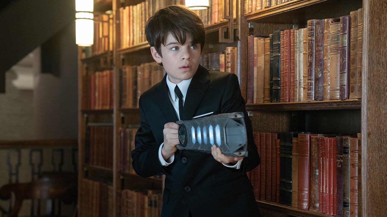 Artemis Fowl (played by Ferdia Shaw) holding a metal object in a library in the movie ARTEMIS FOWL