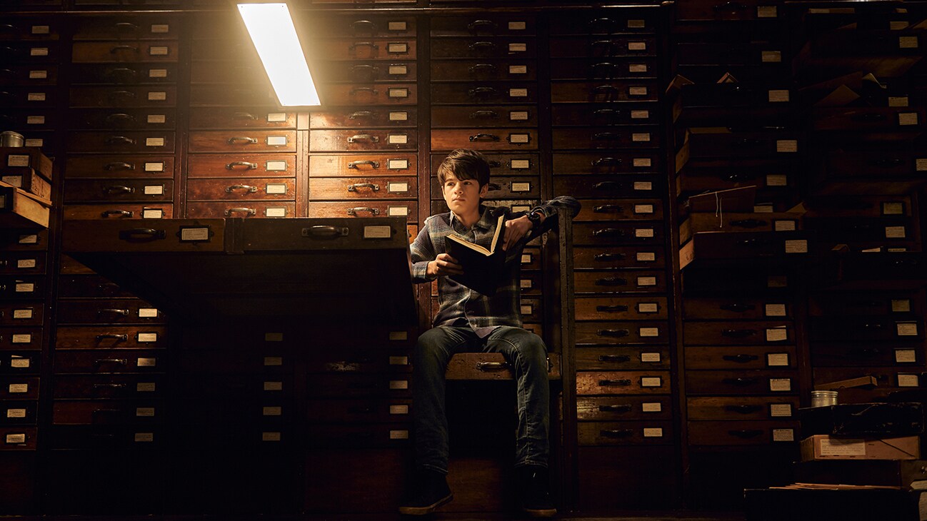  Artemis Fowl (played by Ferdia Shaw) sitting in the library holding a book in the movie ARTEMIS FOWL.