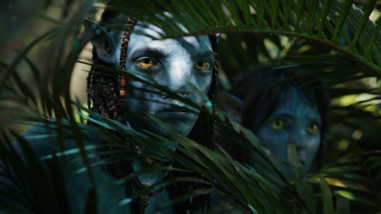 Lo'ak and Kiri peer out from behind some plants.