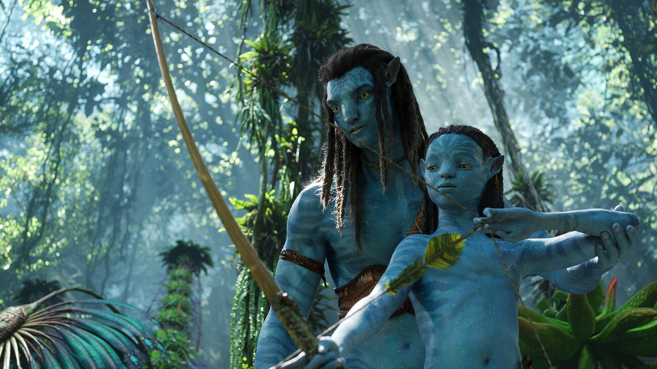 A Na'vi adult next to a Na'vi child with a bow from the 20th Century Studios movie, "Avatar: The Way of Water".