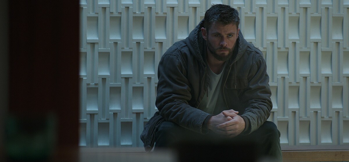 Chris Hemsworth, who plays Thor in Avengers: Endgame, sitting in front of a white textured wall