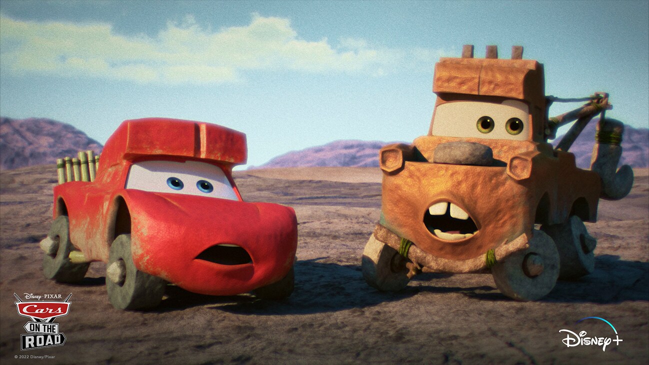 Lightning McQueen (voice of Owen Wilson) and Mater (voice of Larry the Cable Guy) looking pre-historic on an open plain from the Disney+ Original series "Cars on the Road".