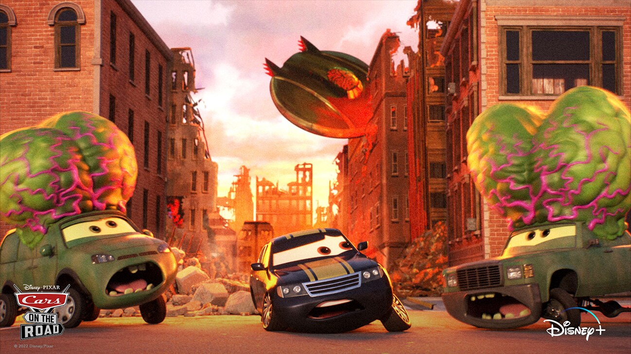 A car in between two cars with oversized alien brains.  A flying saucer has crashed into a building in the background. From the Disney+ Original series "Disney•Pixar Cars on the Road".