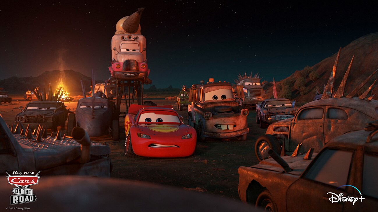 Lightning McQueen (voice of Owen Wilson) and Mater (voice of Larry the Cable Guy) at night surrounded by old and tough looking cars from the Disney+ Original series "Cars on the Road".