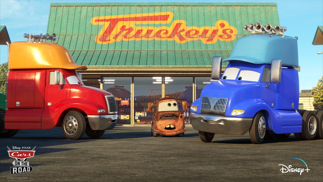 Mater (voice of Larry the Cable Guy) between two big tricks in front of "Truckey's" from the Disney+ Original series "Disney•Pixar Cars on the Road".