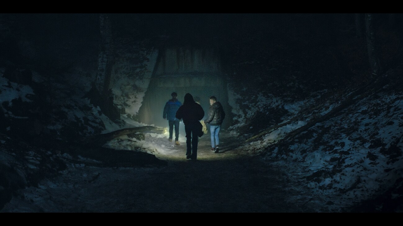 Image of several characters standing in front of a hillside bunker at night from the Disney+ Original series "Parallels".