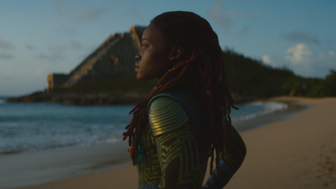 Nakia (actor Lupita Nyong’o) stands at the beach, facing the sea. From the film, Marvel Studios' Black Panther: Wakanda Forever.