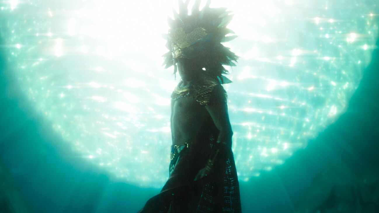 A figure stands clothed in royal clothing in headdress, seemingly underwater. From the film, Marvel Studios' Black Panther: Wakanda Forever.
