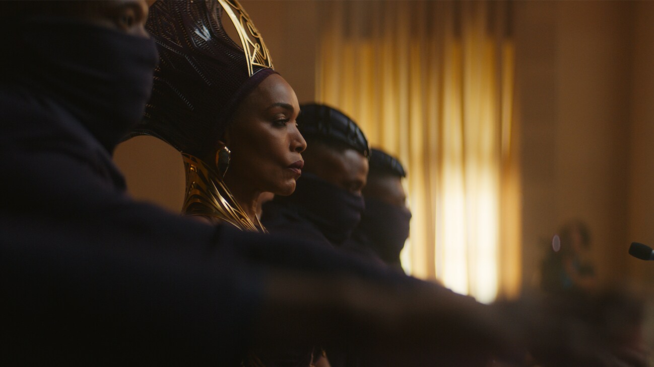 Queen Ramonda (actor Angela Bassett) sits on a panel, with those around her wearing masks up to their eyes. From the film, Marvel Studios' Black Panther: Wakanda Forever.