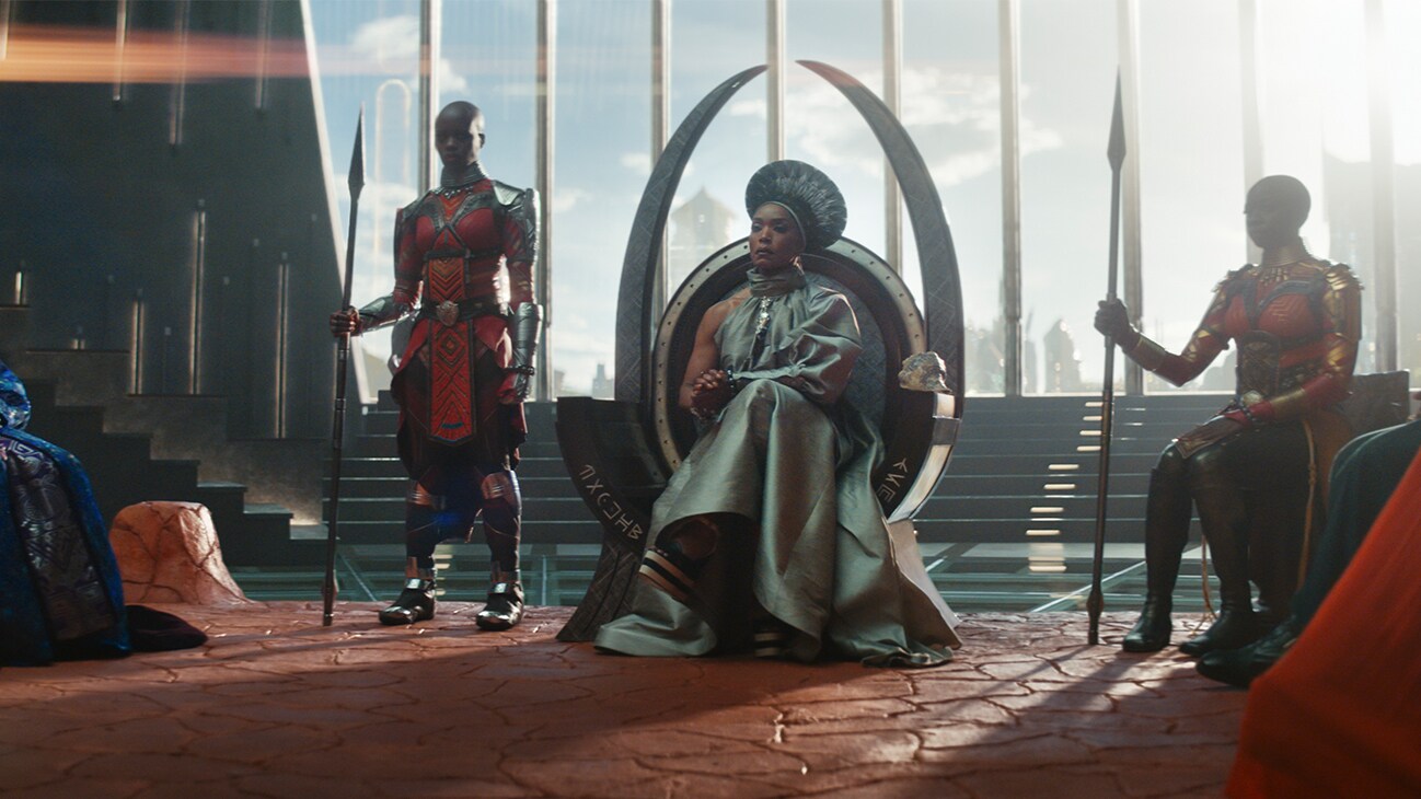 Queen Ramonda (actor Angela Bassett) sits at the throne, with the Dora Milaje and her council around her. From the film, Marvel Studios' Black Panther: Wakanda Forever.