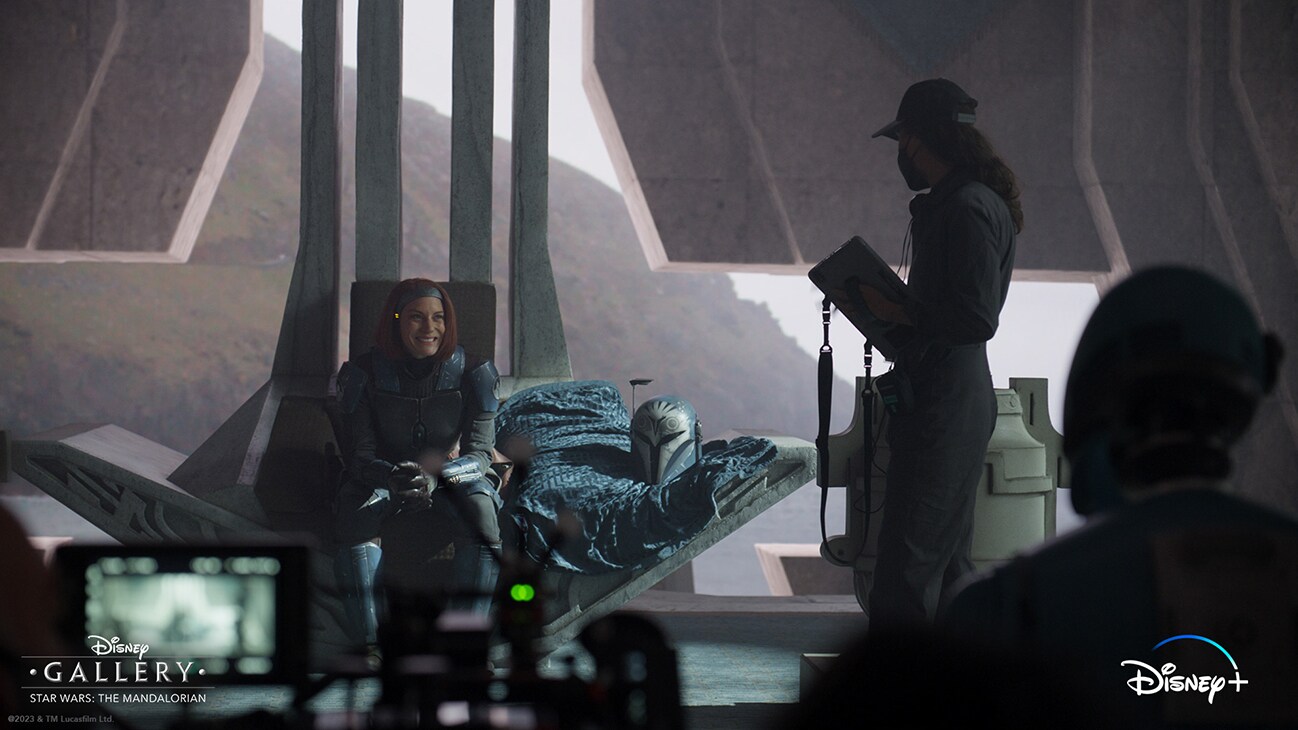 Actor Katee Sackhoff as Bo-Katan Kryze sitting on her throne smiling next to a crew member from the Disney+ Original series, "Disney Gallery - Star Wars: The Mandalorian Season 3."