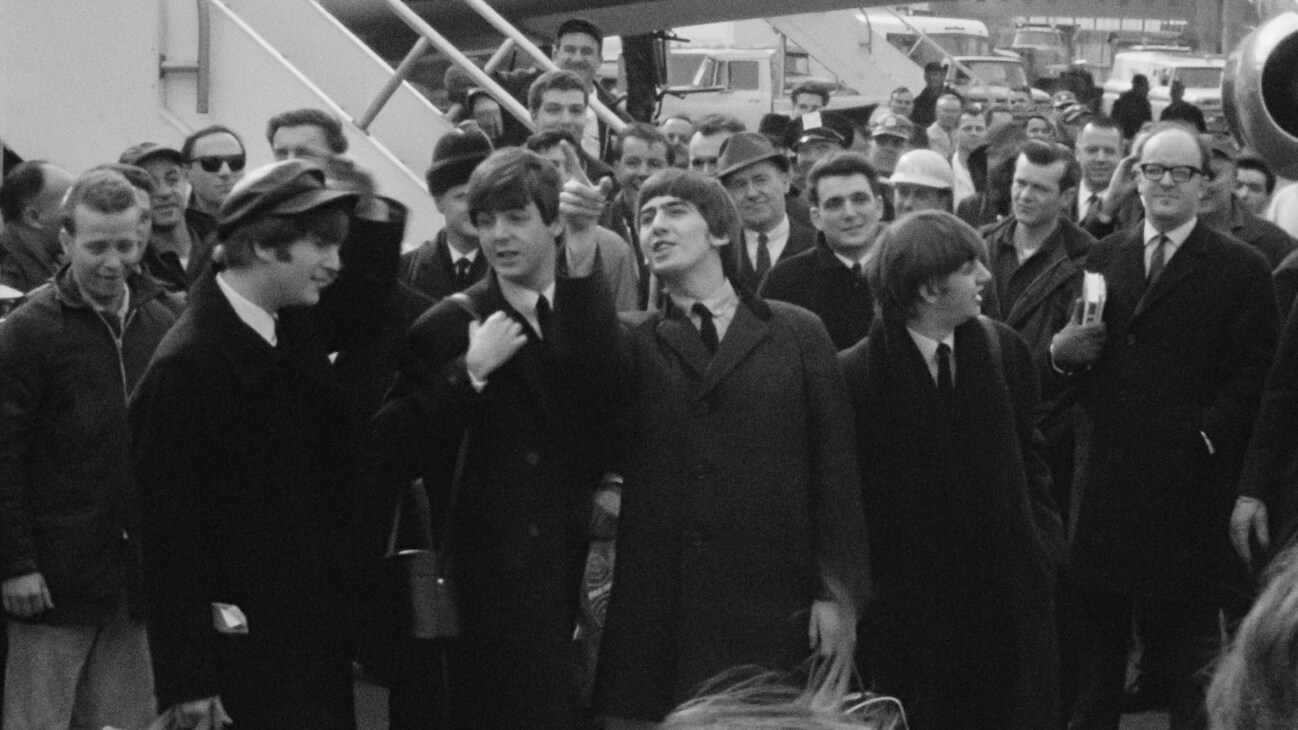 The Beatles departing from their plane to a sea of press in Disney's BEATLES '64. © 2024 Apple Corps, Ltd. All Rights Reserved.