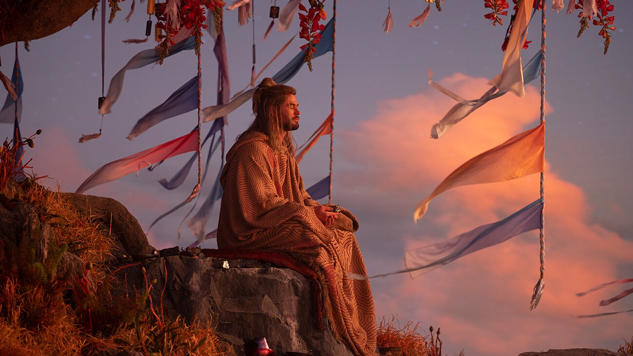 Thor (actor Chris Hemsworth) sits meditating under a big tree with red leaves in Marvel Studios' Thor: Love and Thunder.