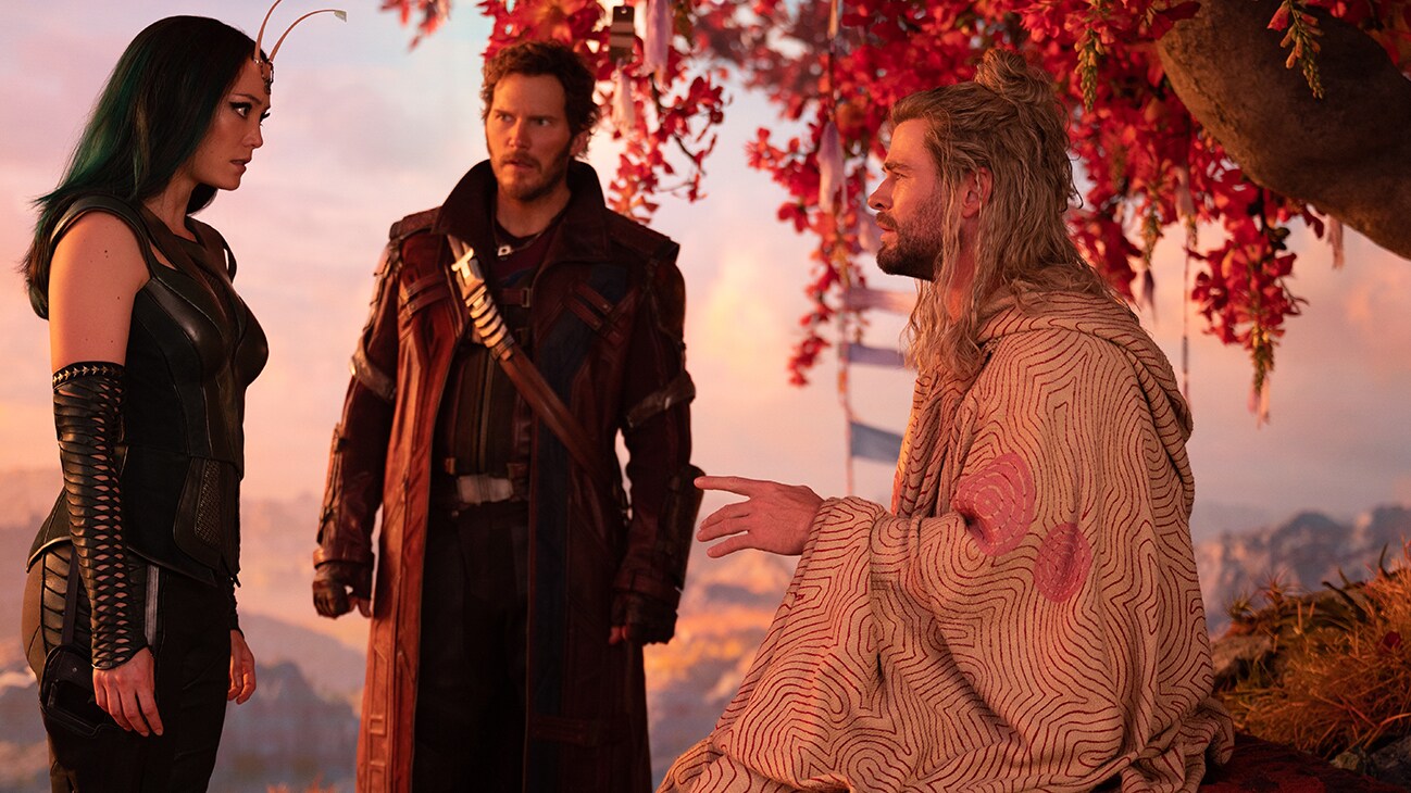Mantis (actor Pom Klementieff), Peter Quill (actor Chris Pratt) and Thor (actor Chris Hemsworth) have a conversation under a big tree with red leaves in Marvel Studios' Thor: Love and Thunder.
