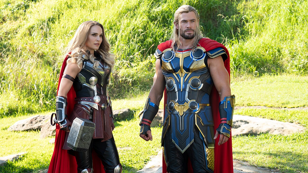 Thor (actor Chris Hemsworth) and Mighty Thor (actor Natalie Portman) stand together in a grassy hillside in Marvel Studios' Thor: Love and Thunder.