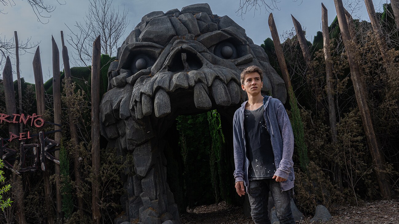 A character from the Disney+ Original series, Tierra Incognita, stands before the entrance to an abandoned theme park attraction in the shape of a skull.