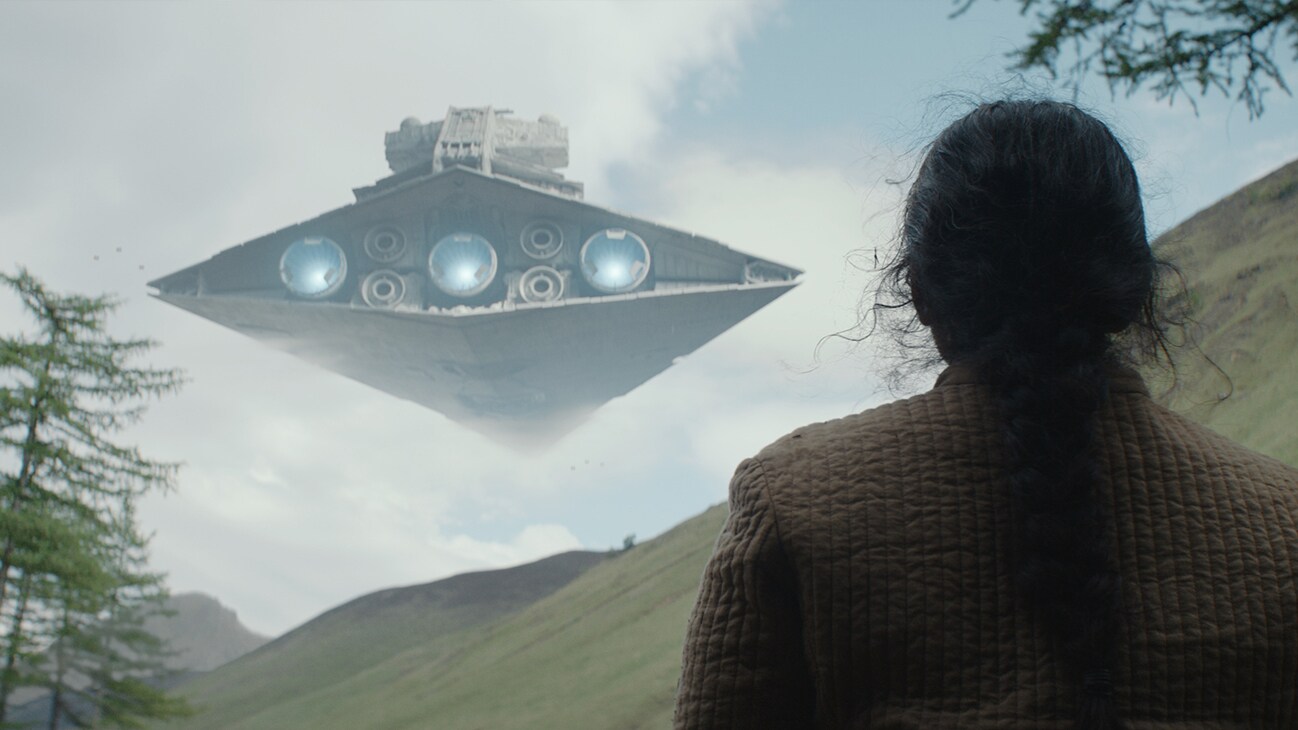 A person looking at an Imperial Star Destroyer flying above a hilltop from the Disney+ Original series, "Andor."