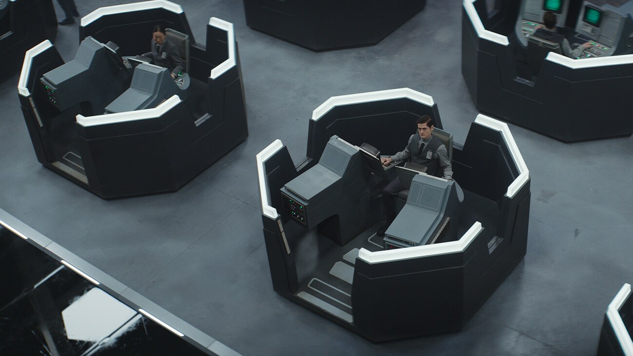 Syril Karn (actor Kyle Soller) sitting at a computer terminal pod from the Disney+ Original series, "Andor."