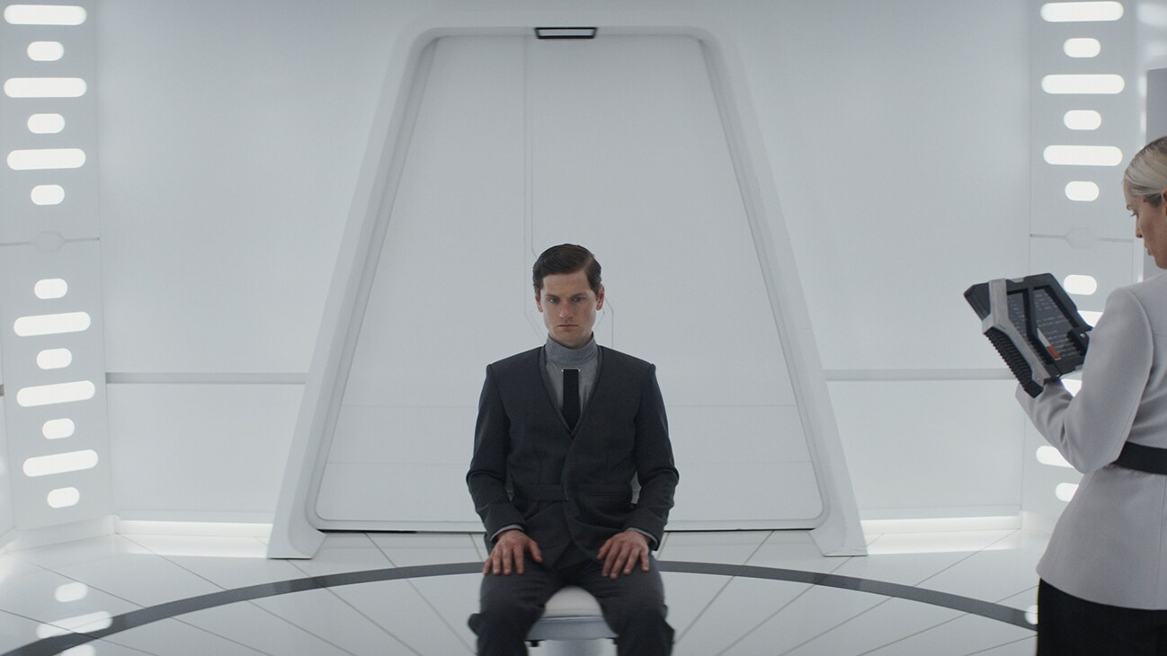 Syril Karn (actor Kyle Soller) sitting in a suit and tie from the Disney+ Original series, "Andor."