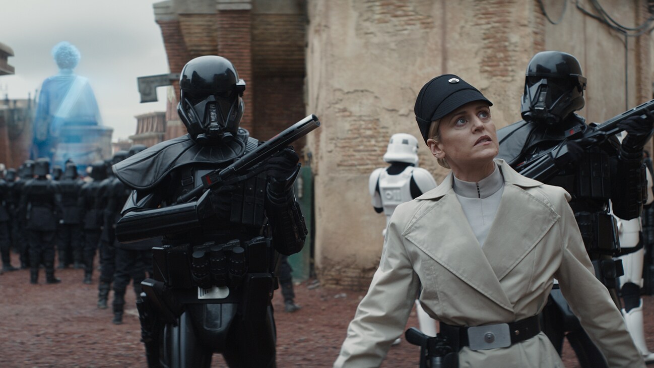 Dedra Meero (actor Denise Gough) and several Imperial Death Troopers walk down a city street from the Disney+ Original series, "Andor."