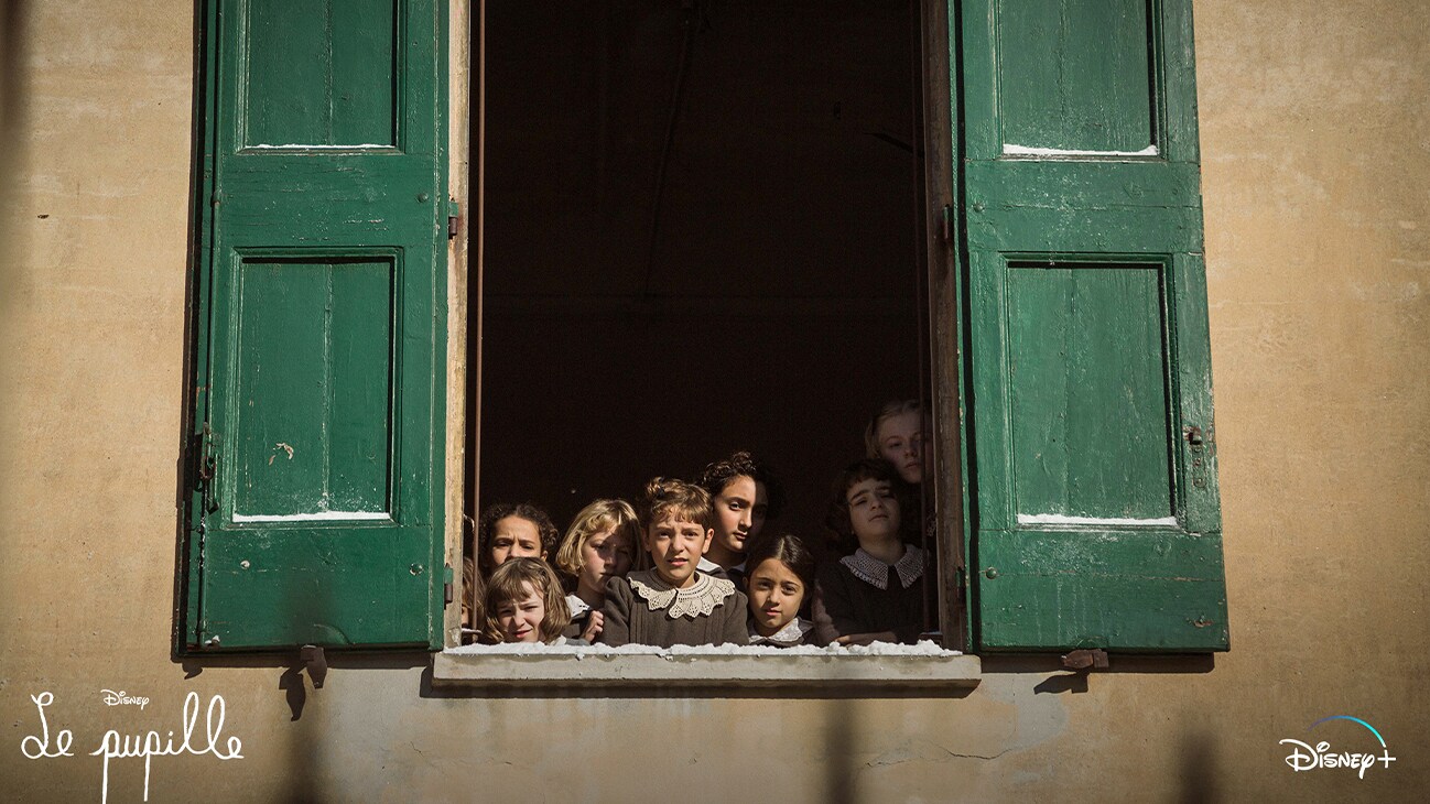Image of children looking out a window with green shutters.