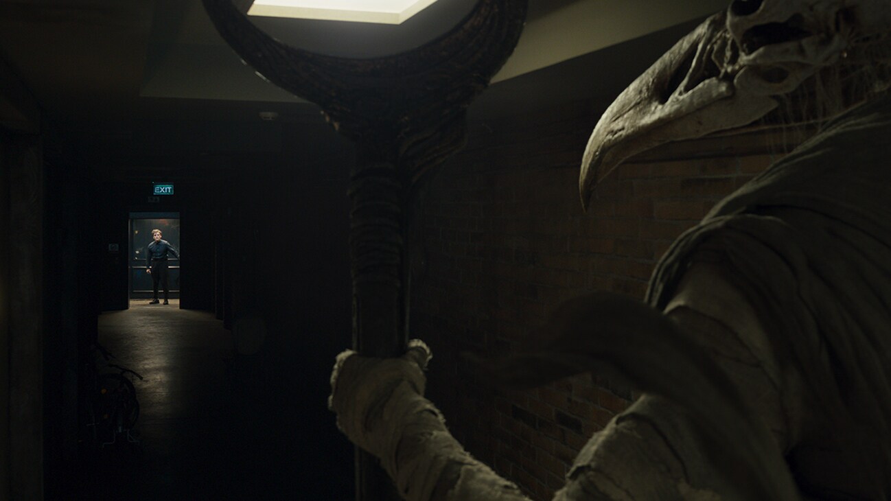 Image of Steven Grant (actor Oscar Isaac) standing in a doorway facing a Khonshu (voiced by F. Murray Abraham) holding a staff from Marvel Studios' "Moon Knight".