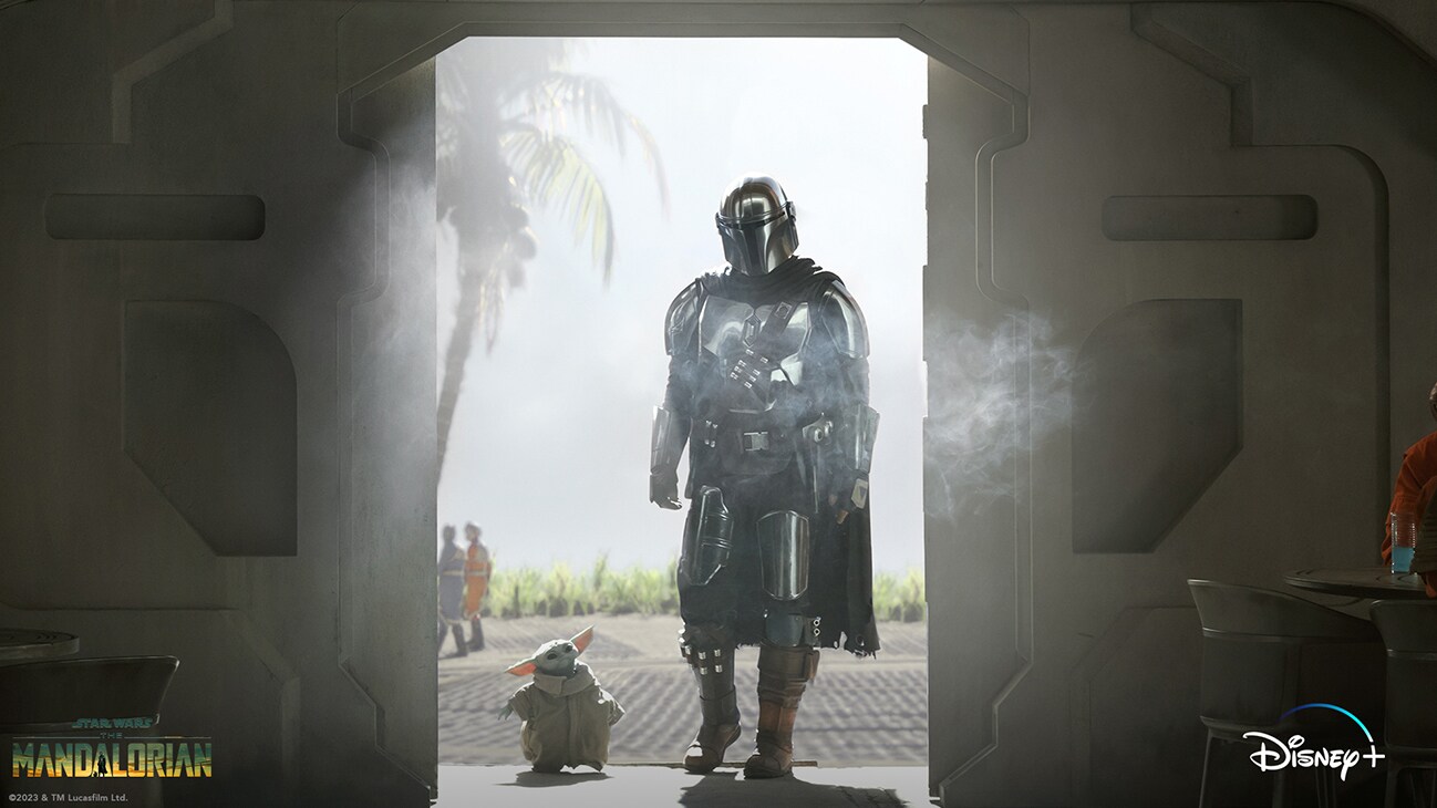 Grogu and The Mandalorian (actor Pedro Pascal) walk though a doorway from the Disney+ Original series, "The Mandalorian."