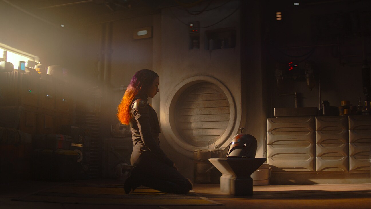Sabine Wren (Natasha Liu Bordizzo) kneeling before a helmet from the Disney+ Original series, Star Wars: Ahsoka.
